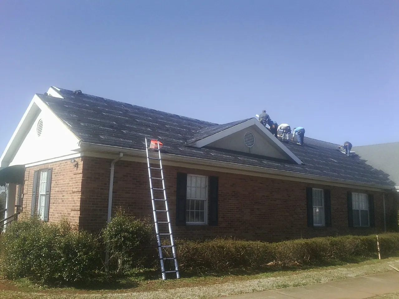 Crew tearing shingles off a brick ranch roof with a ladder set — Metal Roof Repair work by our crew in Kings Mills
