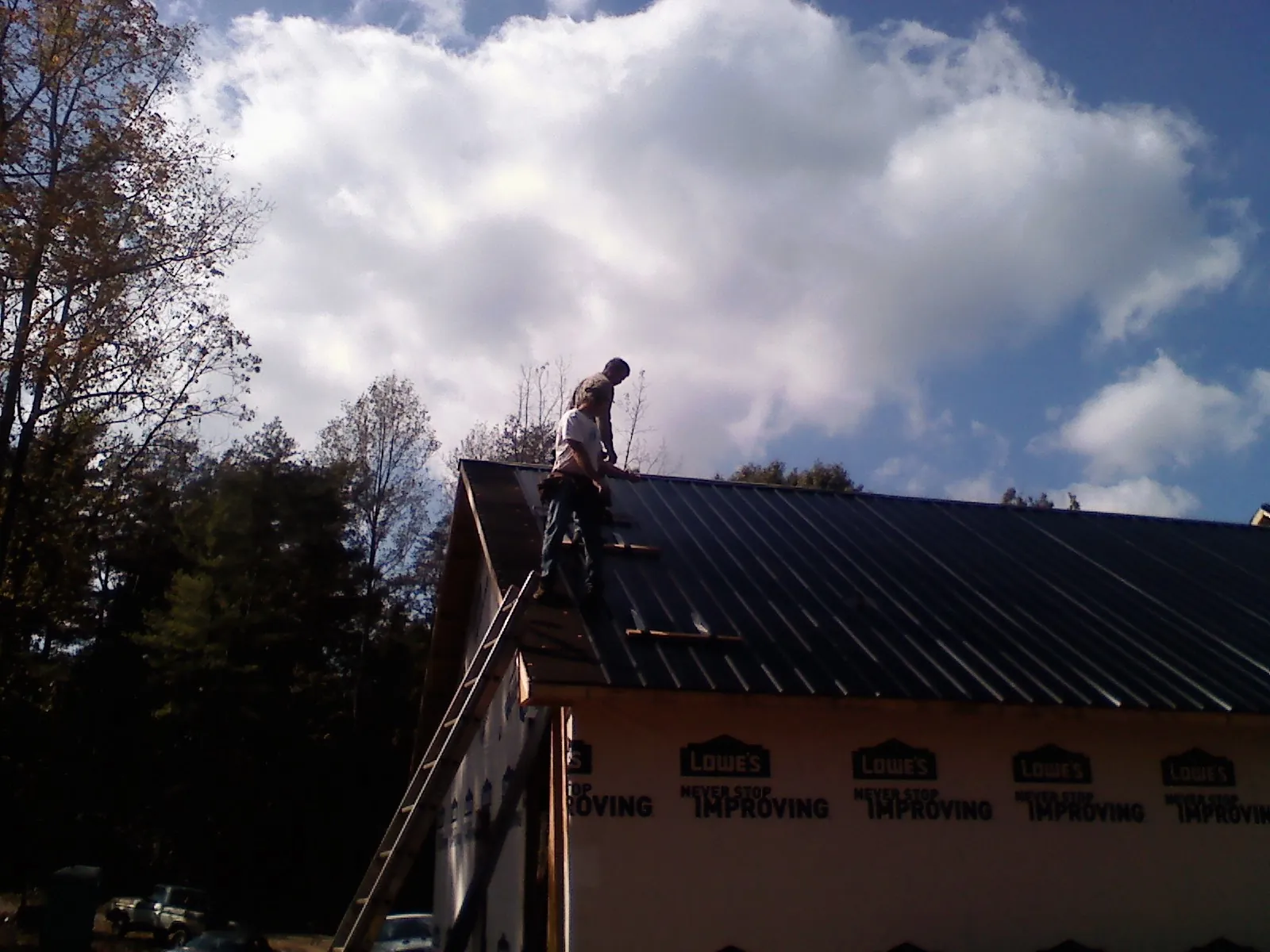 Roofer fastening dark metal panels high against a cloudy sky, from a Roof Inspection job in Kings Mills