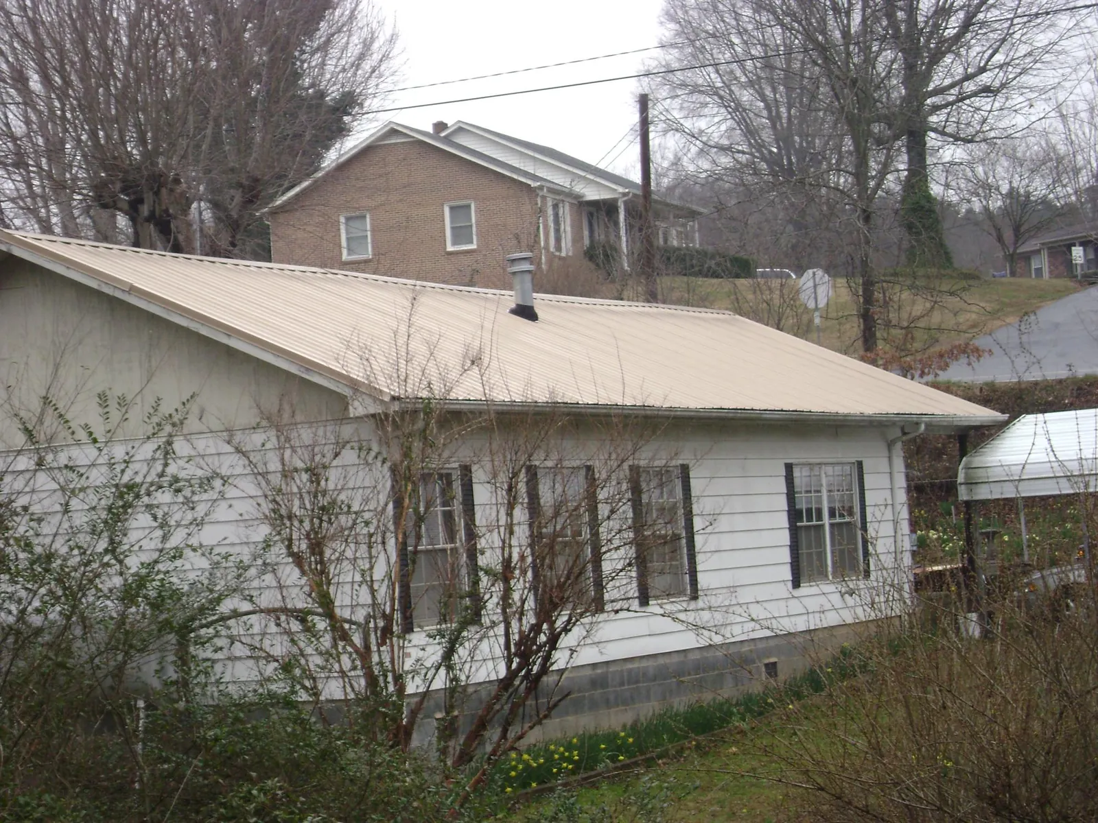 Tan metal roof on a white sided house set into a hillside in Kings Mills